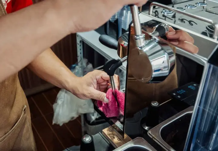 Ręce barista czyszczą dyszę ekspresu, przygotowując go do odkamieniania. Dbałość o sprzęt zapewnia idealne lattego.