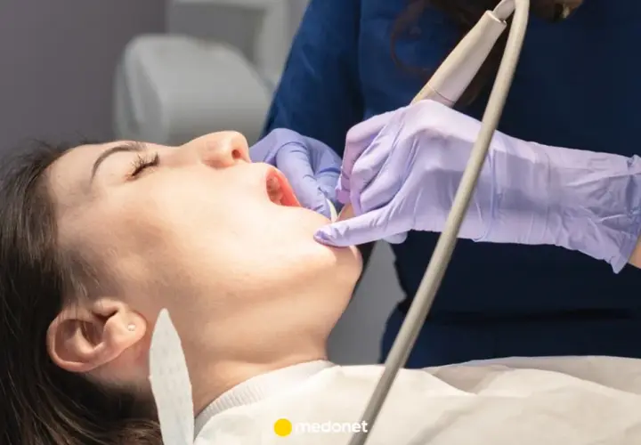 Dentysta w fioletowych rękawiczkach bada ząb pacjentki otwartymi ustami.