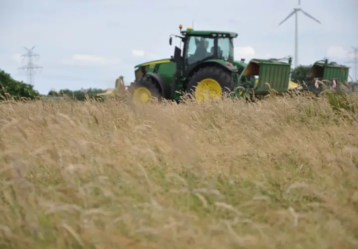Grüner Traktor mit Anhängern im Feld, bereit für die Ernte. Die Kfz-Steuer für diesen Traktor ist ein wichtiger Faktor für Landwirte.