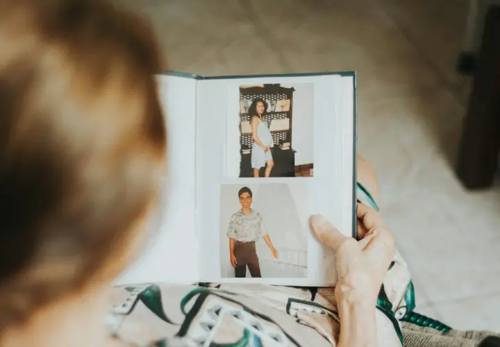 Osoba przegląda fotoksiążkę z dawnymi zdjęciami. Widać ciążowy brzuch i młodego mężczyznę. To inspiracja, jak zrobić fotoksiążkę.