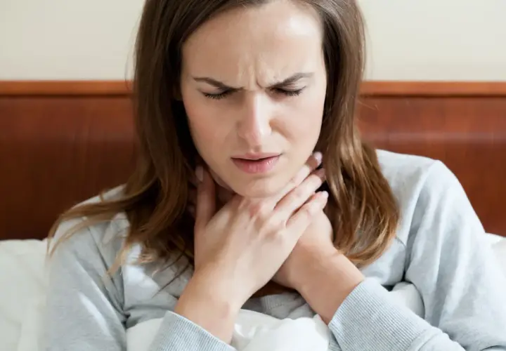 Donna con mani sul collo, espressione sofferente, forse per difficoltà a deglutire o ansia.
