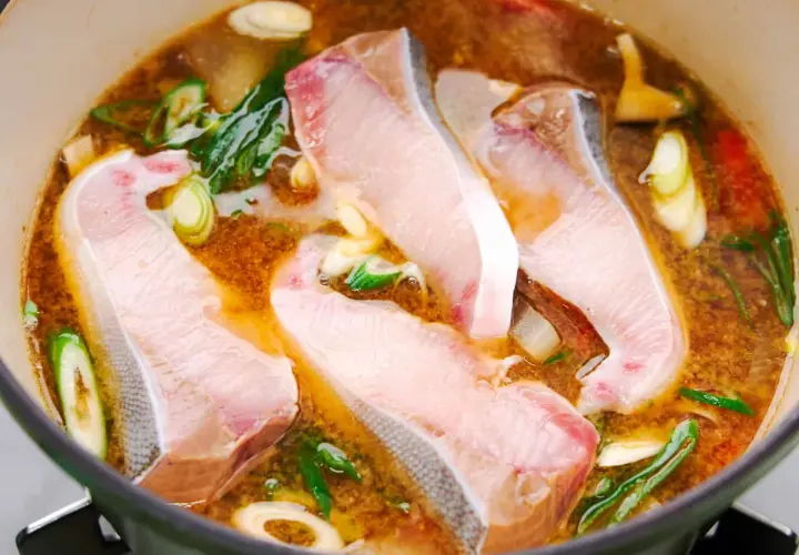 A pot of simmering Japanese fish soup with tender white fish fillets, green onions, and ginger.
