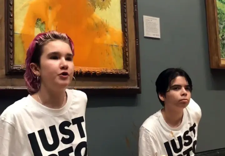 Zwei junge Menschen mit T-Shirts "JUST STOP" vor einem beschmierten Van Gogh Gemälde.