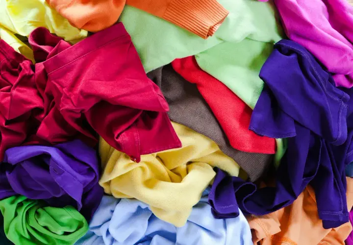 Bunte Stoffe, bereit für T-Shirt Upcycling. Ein Berg aus Rot, Lila, Grün, Gelb und Orange lädt zum kreativen Gestalten ein.
