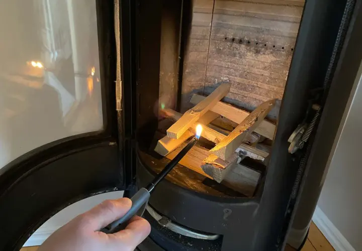 En hand tänder ved i en kamin. Det syns lite tjära i skorstenen.