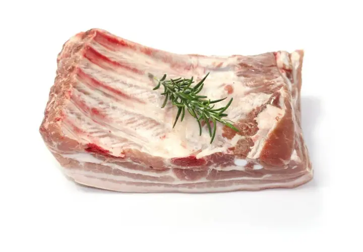 Un morceau de poitrine de porc frais, avec des côtes apparentes et une branche de romarin posée dessus, prêt à être cuisiné.