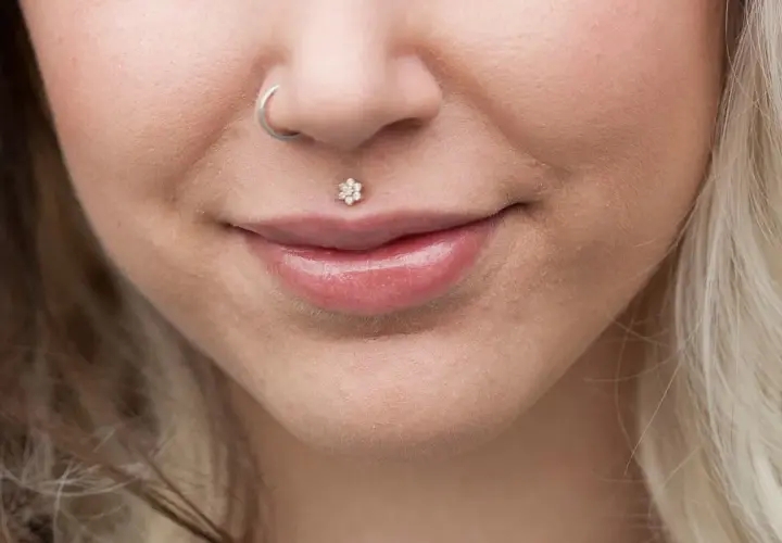 Usta z błyszczącym błyszczykiem i kwiatowym medusa piercingiem. Kolczyk w nosie dodaje uroku.