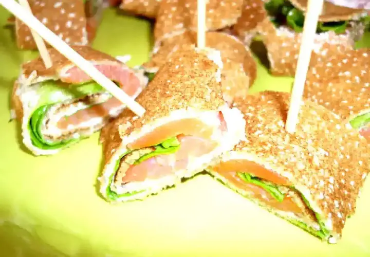 Rouleaux de galette sarrasin garnis de saumon fumé et de salade verte, servis sur une assiette jaune vif.
