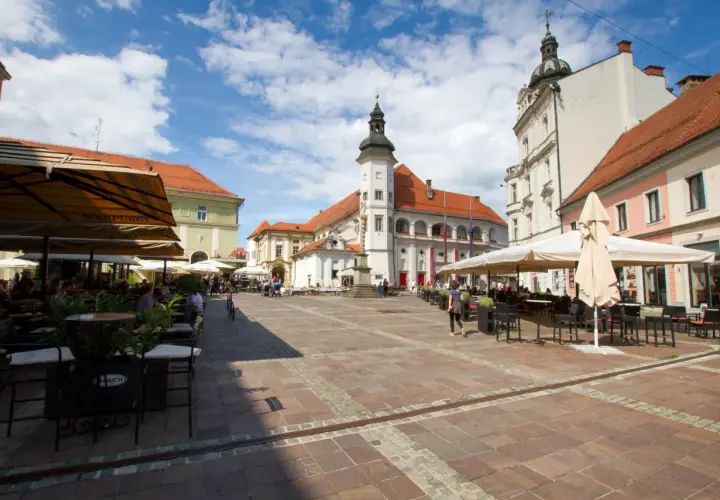 Rynek w Mariborze z kawiarnianymi ogródkami i zabytkowymi budynkami.