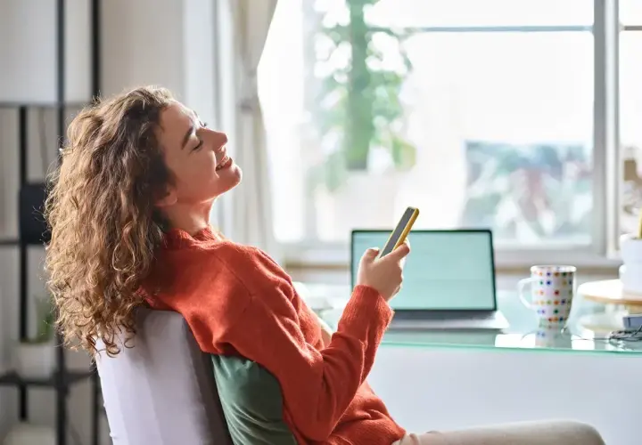 Kobieta z kręconymi włosami śmieje się, trzymając telefon. Czy 3 maja można pracować? Ona chyba odpoczywa.