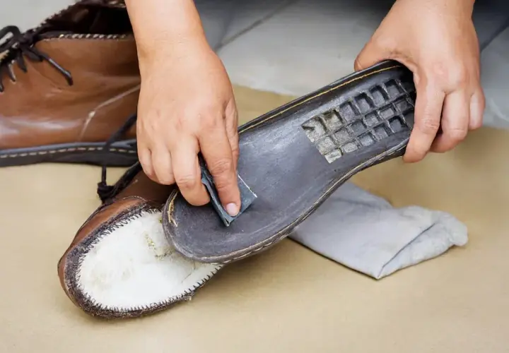 Hands gently sanding the sole of a brown leather boot, demonstrating how to clean Vibram shoes for better grip.