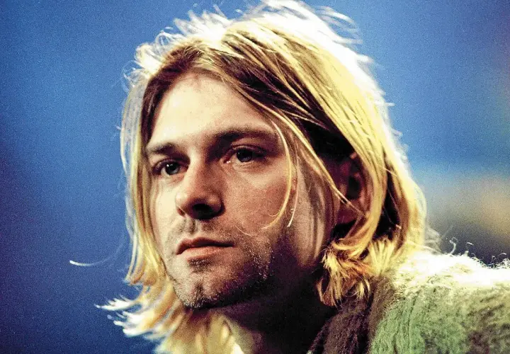 Kurt Cobain, ikona zespołu Nirvana, z charakterystycznymi blond włosami i niebieskimi oczami, na tle niebieskiego tła.