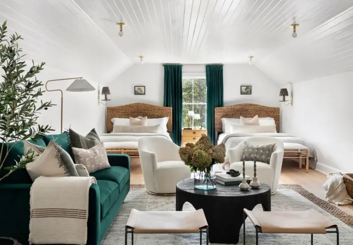 Two beds flank a window with teal curtains. Multiple rugs define the seating and sleeping areas in this cozy room.