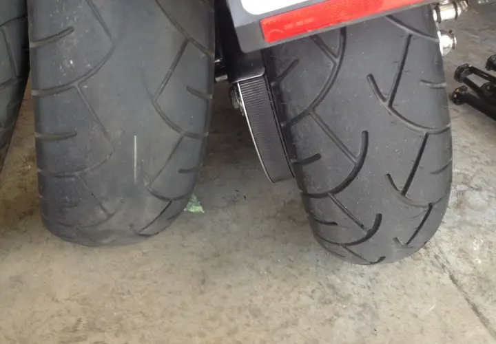 Dos ruedas de moto, una rueda moto gastada con dibujo casi liso y otra con más surcos, sobre suelo de hormigón.