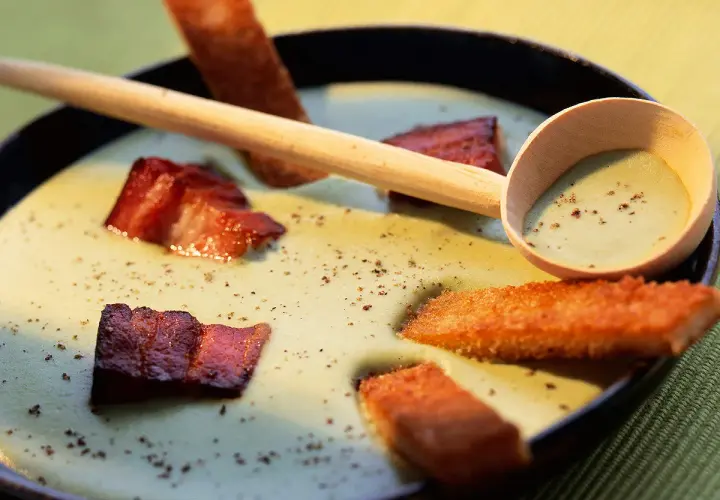 Une cuillère en bois sert une soupe de pois cassés onctueuse, garnie de lard croustillant et de croûtons dorés.