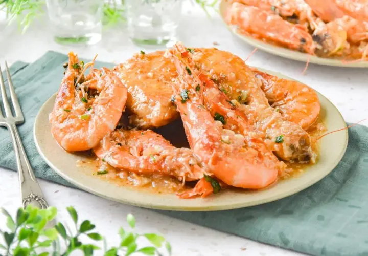 Plato de pollo con gambas en salsa de ajo y perejil, servido en un plato beige con un tenedor a la izquierda.
