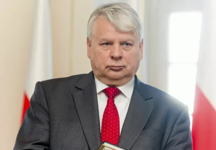 Bogdan Borusewicz w garniturze i czerwonym krawacie, na tle flagi Polski.
