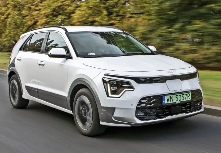 Biały Kia e-Niro jedzie po drodze, otoczony zielenią drzew.