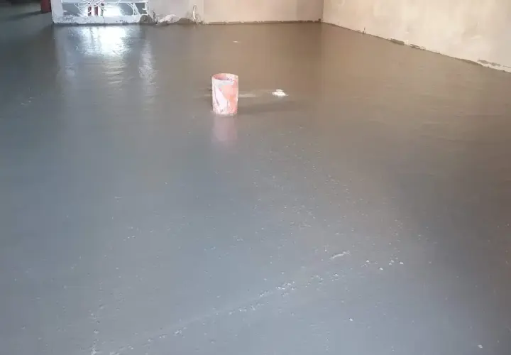 Świeżo wylany, gładki **pianobeton** na podłodze. W tle widać wiaderko i instalacje.