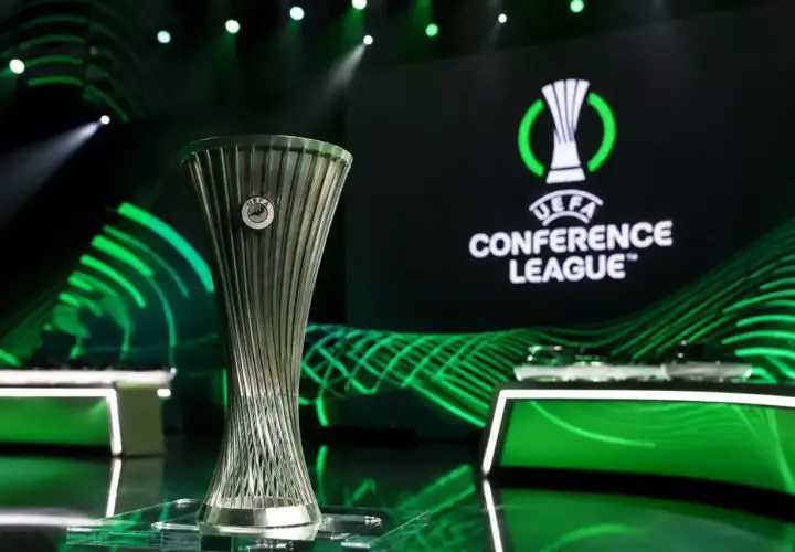 Trofeum Ligi Konferencji UEFA na tle logo i zielonych świateł. Marzenie o wygraniu tych rozgrywek napędza emocje podczas meczów ligi konferencji.