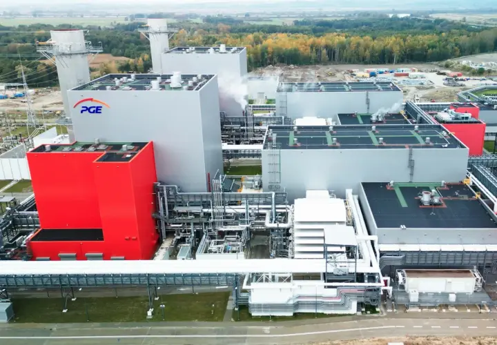 Nowoczesna elektrownia PGE z czerwonym budynkiem i białymi blokami, w tle las i kominy.