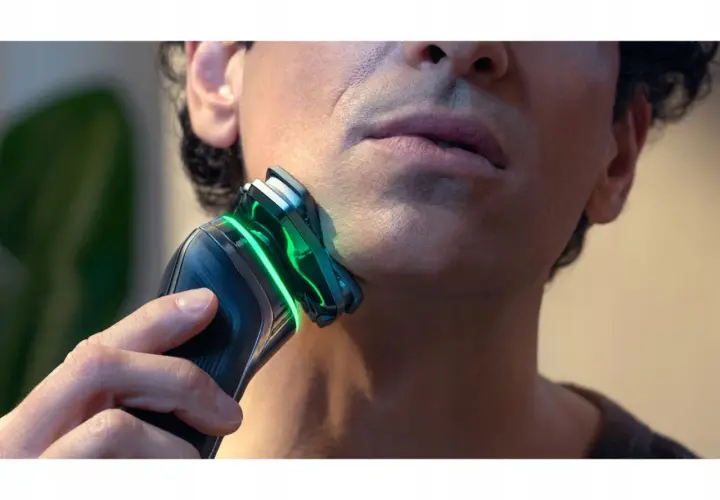 Mężczyzna goli twarz golarką Philips z zielonym podświetleniem.