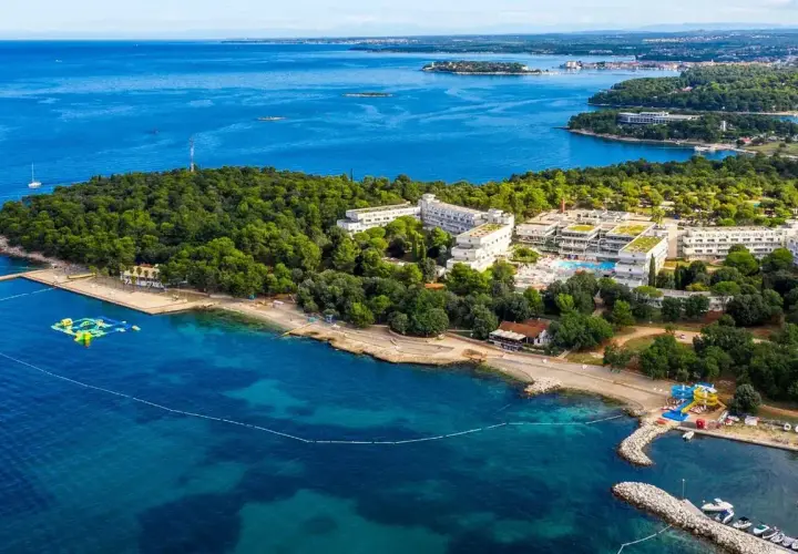 Hotel Delfin Plava Laguna, otoczony zielenią, z basenami i plażą nad turkusowym morzem.