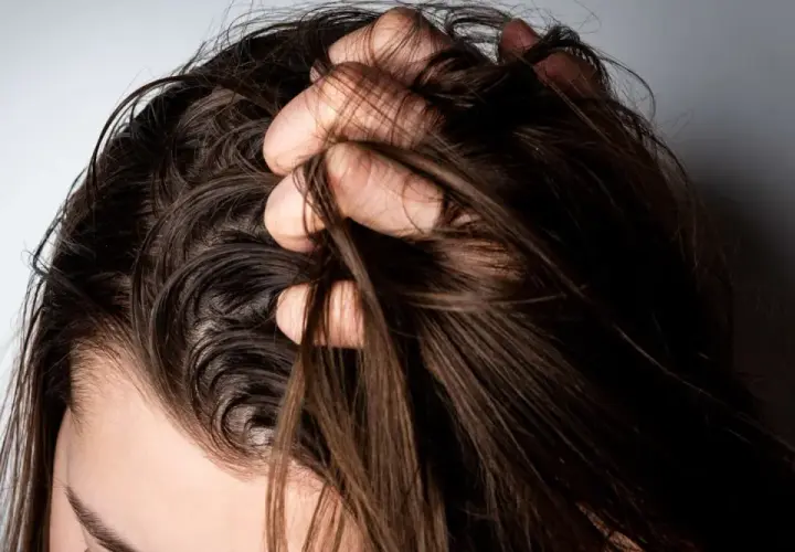 Mano revolviendo cabello oscuro y lacio. ¿Es mejor teñirse con el pelo sucio o limpio?