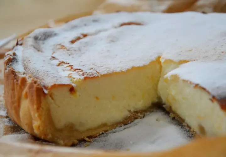 Une part de tarte à la ricotta sucrée, saupoudrée de sucre glace, révèle sa garniture crémeuse et sa croûte dorée. Un délice !