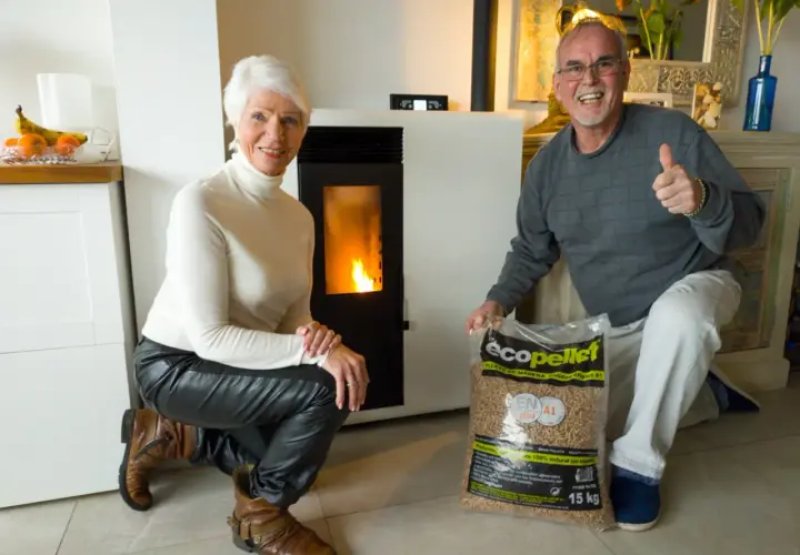 Pareja feliz junto a su nueva estufa de pellets, con una bolsa de combustible lista para la instalación.