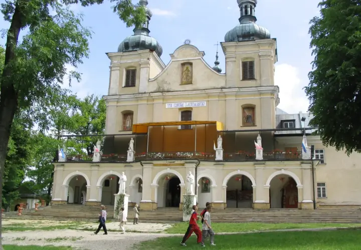 Kalwaria Pacławska: Sanktuarium z kopułami i tarasem, gdzie pielgrzymi spacerują pośród zieleni.