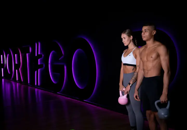 Para dwojga z kettlebellami na tle neonowego napisu "PORT#GO".