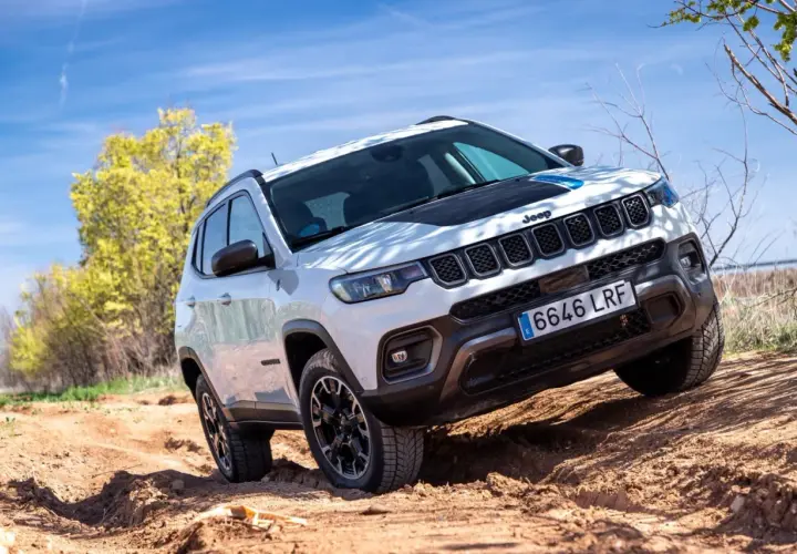 El Jeep Compass Trailhawk 4xe blanco se aventura por un camino de tierra, demostrando su capacidad todoterreno bajo un cielo azul.