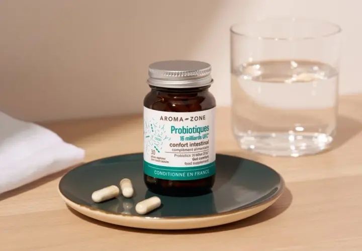 Bouteille de probiotiques Aroma-Zone sur une assiette avec des gélules, à côté d'un verre d'eau. Une cure probiotique pour le confort intestinal.