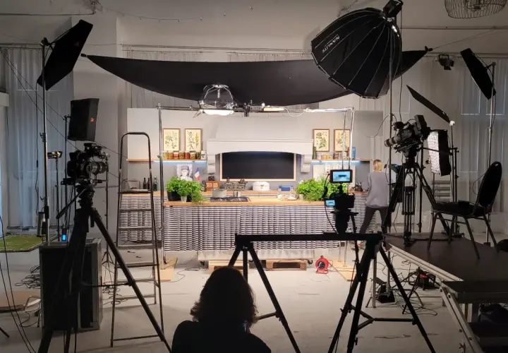 Studio filmowe z kuchnią, kamerami i lampami. Widać tu moc światła, które tworzy atmosferę do nagrania.