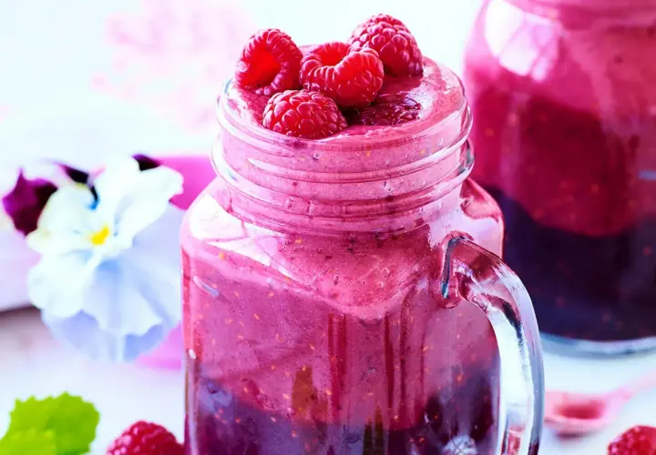 En härlig hallonsmoothie i ett glas med färska hallon på toppen. Ett perfekt smoothie recept för en solig dag.
