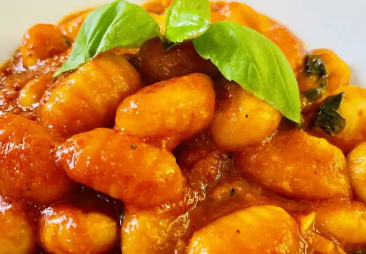 Gnocchi al pomodoro, soffici e avvolti in un sugo rosso brillante, guarniti con foglie di basilico fresco.