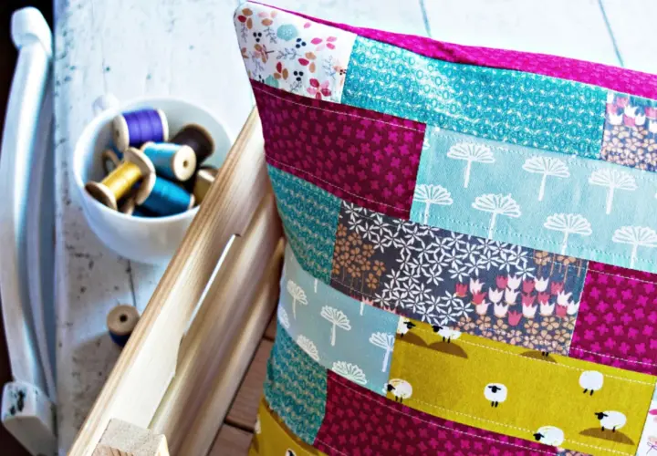 Buntes Patchwork-Kissen zeigt, wie man Stoffreste sinnvoll verwerten kann. Kleine Schafe und Blumenmuster zieren die Kissenhülle.