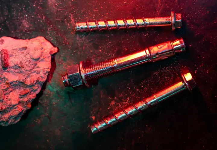 Tasselli e bulloni metallici, con un pezzo di cemento grezzo. La scena è illuminata da luci rosse e verdi, creando un'atmosfera drammatica, ideale per una tabella portata tasselli.