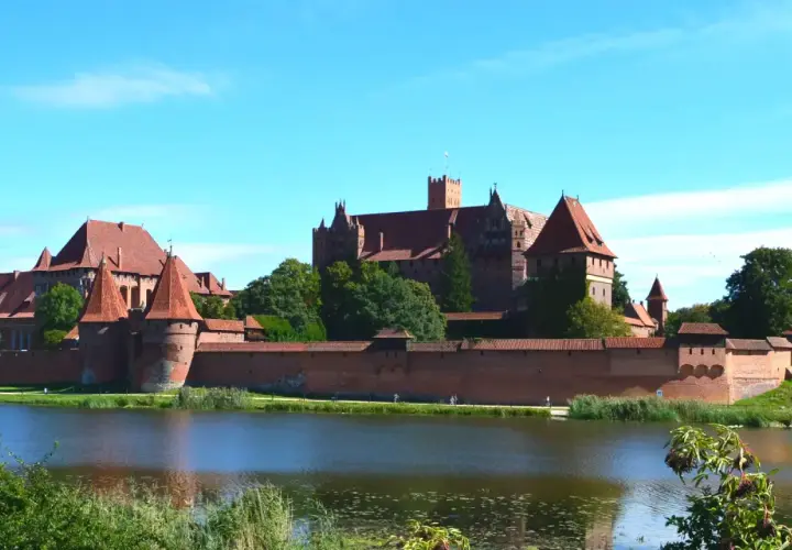 Potężny zamek Malbork z czerwonej cegły, otoczony murami obronnymi, góruje nad spokojną wodą.
