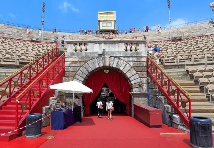 L'Arène de Vérone, avec ses gradins de pierre et ses escaliers rouges, accueille des visiteurs sous un ciel bleu.
