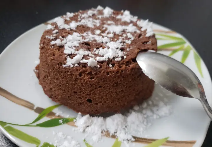 Un délicieux bowl cake au chocolat, saupoudré de sucre glace, prêt à être dégusté avec une cuillère.