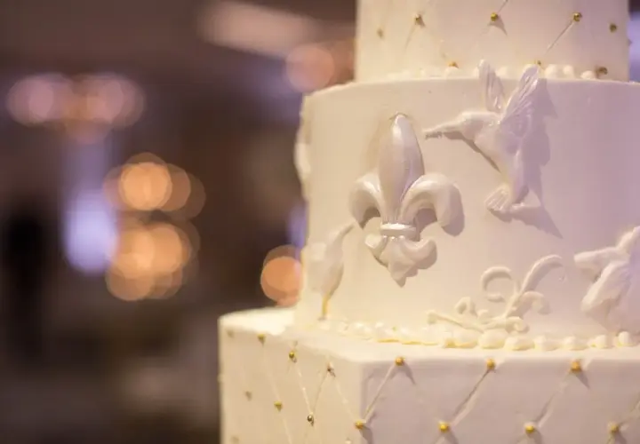 Elegancki tort weselny z ozdobami z masy cukrowej, jak przykleić ozdoby z masy cukrowej do tortu? Delikatne lilie i ptaszki zdobią białe warstwy.