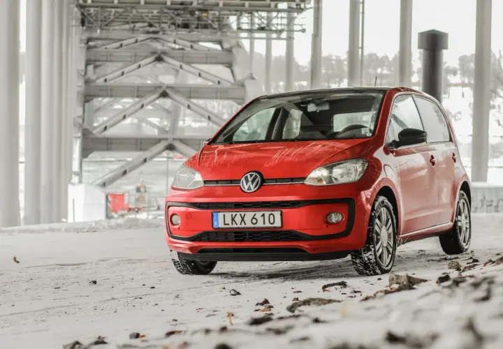 Röd VW Up med vinterdäck står på snöig mark under en bro. Ett vw up problem kan vara att den fastnar i snön.