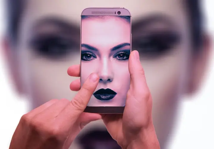 Dłonie trzymają smartfon, na ekranie którego widać twarz kobiety z mocnym makijażem. To przykład zaawansowanej fotografia obliczeniowa.