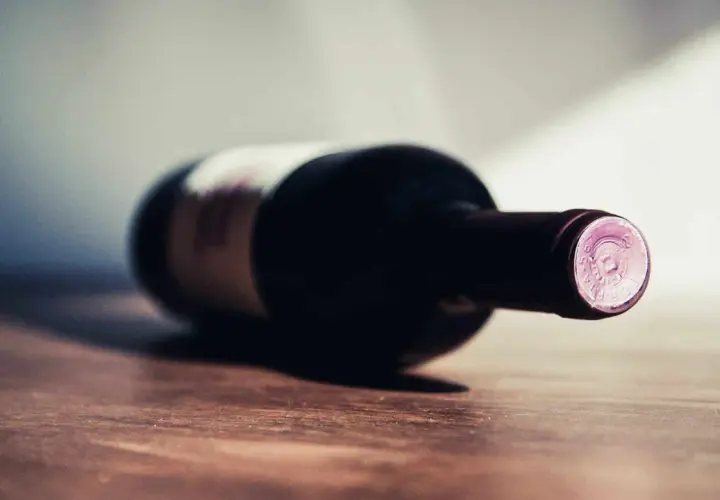 Une bouteille de vin couchée sur une table en bois. La question se pose : 1 bouteille de vin pour combien de personnes ?