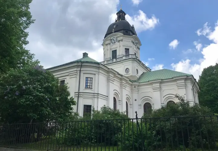 Adolf Fredriks kyrka i Stockholm, en vit kyrka med grön kupol och tak, omgiven av träd och buskar.