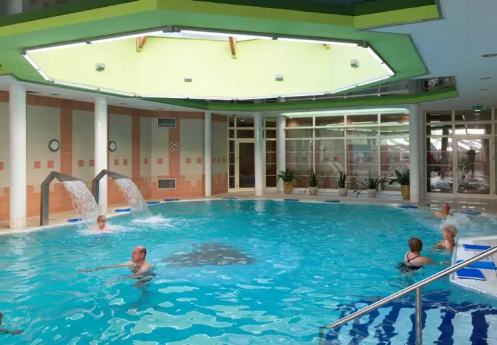 Basen rehabilitacyjny z hydromasażem i wodospadami, w którym kąpią się ludzie.