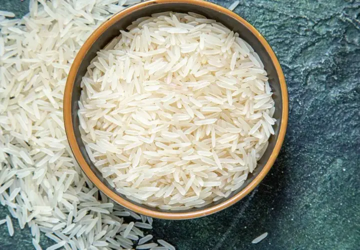 Chicchi di riso basmati in una ciotola e sparsi su una superficie scura. Le proprietà del riso basmati lo rendono un alimento leggero e digeribile.