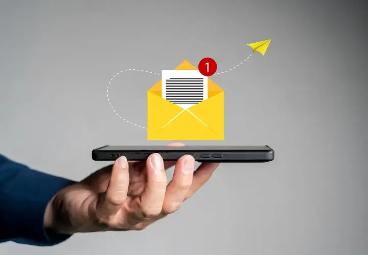 Dłoń trzyma smartfon, z którego wylatuje żółta koperta z powiadomieniem. Pomysł na to, co napisać w SMSie o urlop na żądanie.